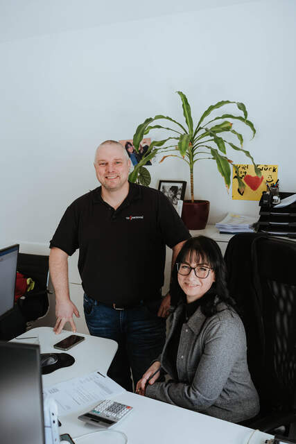 Zwei Mitarbeitende entspannt im Büro im Austausch Zwei Mitarbeiter diskutieren gemeinsam an einem Schreibtisch, arbeiten konzentriert und tauschen sich ruhig über ein Thema aus.